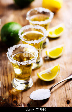 Golden mexican tequila in shot glass with lime and salt on vintage wooden table. Nightlife cocktail drinks menu. Closeup of alcohol beverage in pub. Stock Photo