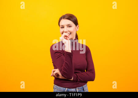 Charming caucasian woman smiling and bitting her thumb over yellow background. Attractive woman. Stock Photo