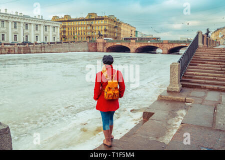 Blonde in a red coat walks along the embankment of the Fontanka River. St. Petersburg, Russia - March 15, 2019. Stock Photo