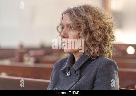 Religious woman sitting alone in a church pew looking ahead towards the altar deep in spiritual thought and praying Stock Photo