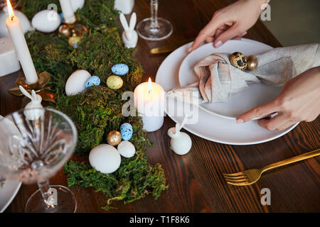 cropped view of woman putting plates near burning candles and moss on wooden table at home Stock Photo