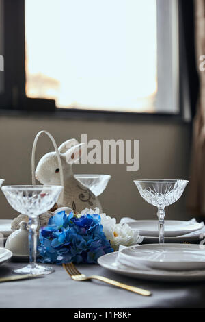plates, crystal glass, decorative bunnie and flowers on table at home Stock Photo