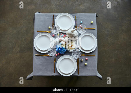 top view of table with white plates, cutlery, crystal glasses, cutlery, painted eggs and flowers at home Stock Photo