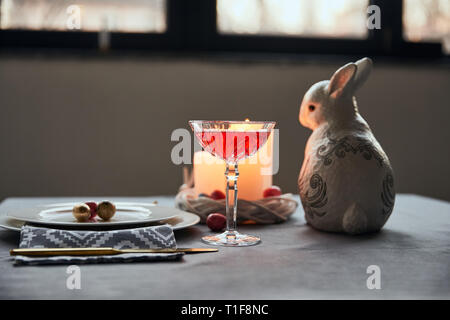 selective focus of decorative bunnie, plates with eggs, wine in crystal glass, candles on table at home Stock Photo