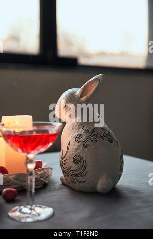 decorative bunnie, eggs, wine in crystal glass and burning candles on table at home Stock Photo