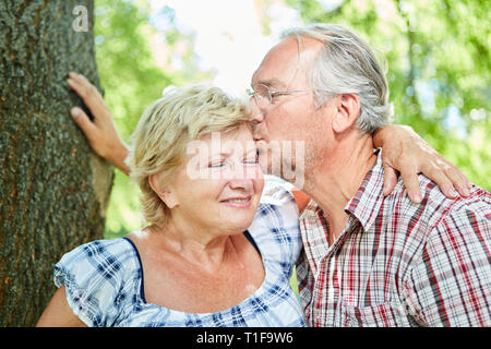 In love senior gives his girlfriend a kiss in nature in summer in dating Stock Photo