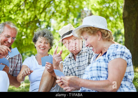 Group seniors as retirees and friends have fun playing cards in the park Stock Photo