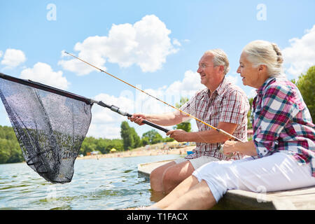 Senior couple with fishing tackle and landing net while fishing together in the summer by the lake Stock Photo