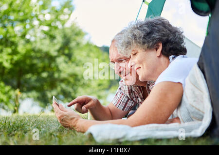 Senior couple using tablet computer online while camping at summer campsite Stock Photo