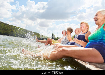 Vital seniors splashing with their feet in the water in the lake in summer vacation Stock Photo