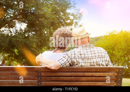 Happy couple of seniors in love sits on park bench in autumn Stock Photo