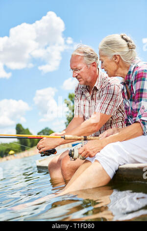 Senior couple sitting together while fishing on the lake in the summer with their feet in the water Stock Photo