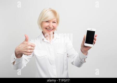 A picture of mature woman with new smartphone. She has tested it and admitted this phone is a good one. That's why she shows a big thumb up. Isolated Stock Photo