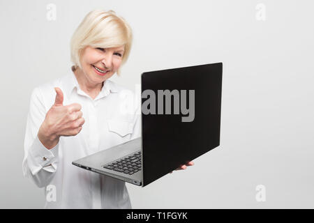 Old but modern woman is holding a new laptop. She likes to use it. The lady prefers to know evetything about new technologies and the last news about Stock Photo