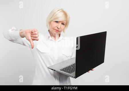 A picture of mature lady with new laptop. She has tested it and admitted the laptop is bad. That's why she shows a big thumb down. Isolated on white Stock Photo