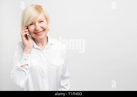 A picture of old lady using new phone. She likes to test it. This phone is her favourite one. Isolated on white background. Stock Photo