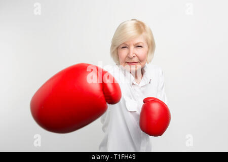 Serious woman is standing in position, wearing red boxing gloves. She is ready for doing some exercises. Isolated on white background. Stock Photo