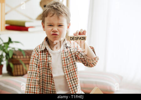 Wooden cubes with word despair in hands of little boy at home. Conceptual image about education, childhood and social problems. Stock Photo