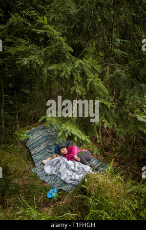 Tho girls resting at a camp under a pine tree in the forest. Stock Photo