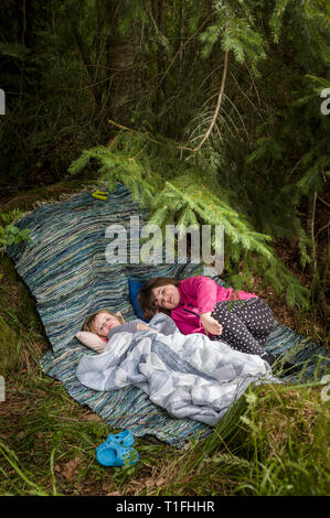 Tho girls resting at a camp under a pine tree in the forest. Stock Photo