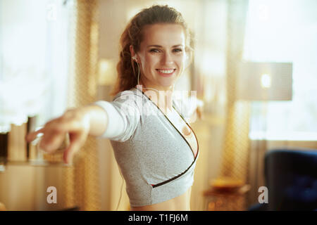 Portrait of smiling young sports woman in fitness clothes listening to the music with headphones and doing dance fitness in the modern house. Stock Photo