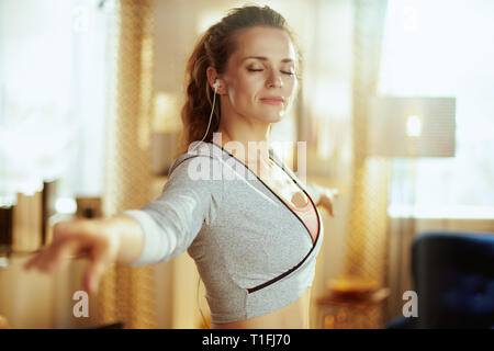 relaxed young woman in sport clothes listening to the music with headphones and doing dance fitness in the modern living room. Stock Photo