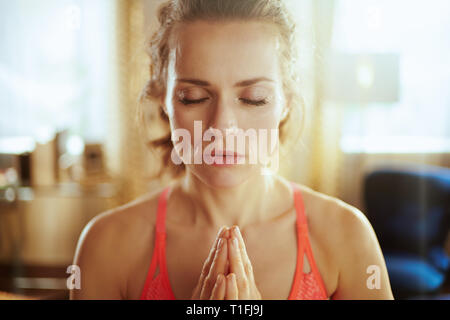 Portrait of relaxed young sports woman in fitness clothes at modern home meditating. Stock Photo