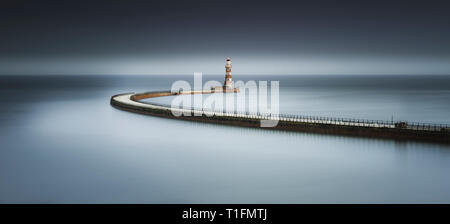 A moody Fine Art colour long exposure of Roker Pier at sunset with the long sweeping path giving a soft mirror reflection in the North Sea Stock Photo