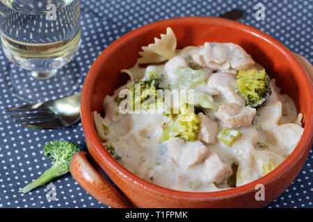 Farfalle pasta with broccoli, chicken meat and cream sauce in earthenware bowl served with white wine on polka dot table cloth Stock Photo