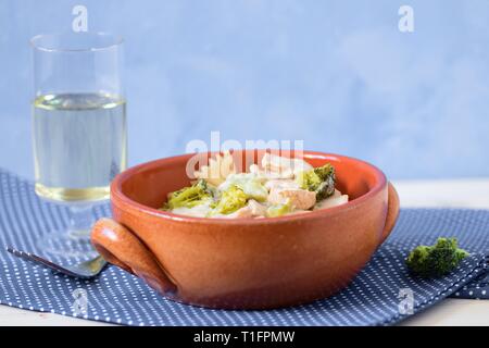 Pasta (farfalle) with broccoli, chicken meat and cream sauce in earthenware bowl served with white wine on polka dot table cloth. Healthy simple lunch Stock Photo