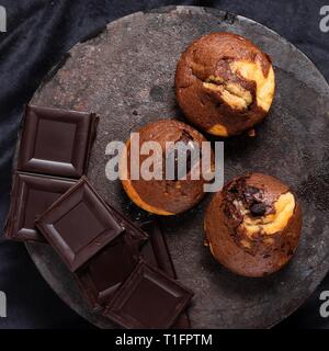 Top down view on three marble muffins and a pile of chocolate on round cast iron tray Stock Photo
