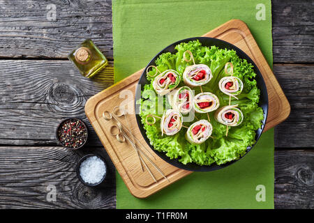 overhead view of sliced sandwich wraps on skewers. roll-ups of whole grain flatbread with yogurt sauce, ham, cheese, lettuce, pepper served on a black Stock Photo