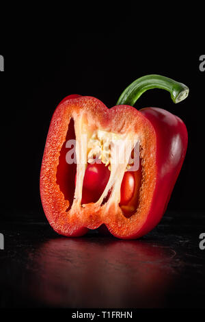 Food photo of a cut red pepper on a black slate plate exposing the inner structure. Stock Photo