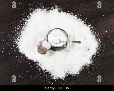 top view of old silver salt cellar with spoon, raw natural Halite mineral and grained Rock Salt on dark brown wooden board Stock Photo