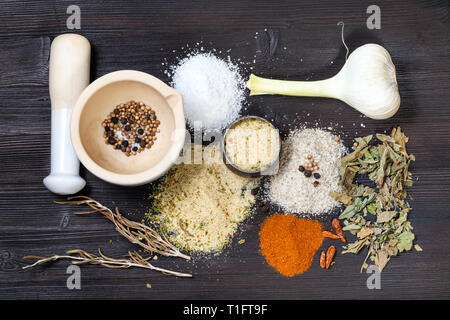 top view of various Seasoned Salts with ingredients and mortar on dark brown wooden board Stock Photo