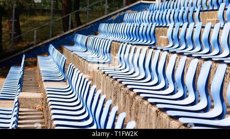 Several rows of empty terraced blue plastic seats in stands of outdoor sports or culture venue Stock Photo