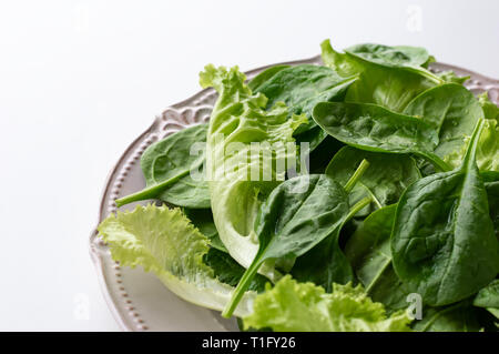 A mixture of spinach leaves and salana leaves on a plate. Selective focus, white background Stock Photo