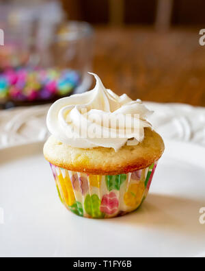 Freshly frosted mini cupcake on a white plate.  Decorating sprinkles in the background. Stock Photo