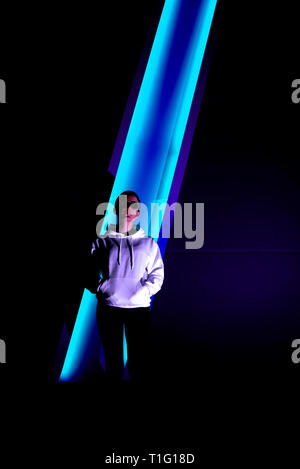 Colorful portrait of a young short haired woman wearing shiny sunglasses and standing in neon lights. Stock Photo