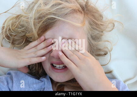 Portrait of a tired child in pain with her hands in front of her eyes Stock Photo