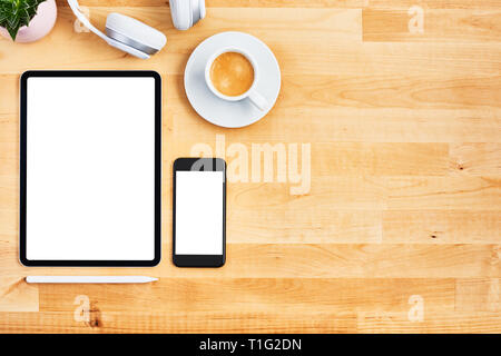 Digital tablet and smartphone with blank white screen, pen, wireless headphone, cup of coffee and plant on wooden office desk. Top view. Copy space fo Stock Photo