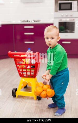 Little boy holds a grid with oranges. Little kid in casual wear carrying child plastic shopping trolley. Shopping, discount, sale concept Stock Photo