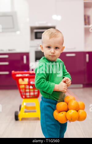 Little boy holds a grid with oranges. Little kid in casual wear carrying child plastic shopping trolley. Shopping, discount, sale concept Stock Photo