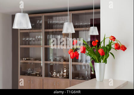 Vase of red flowers on counter by shelves of glassware Stock Photo