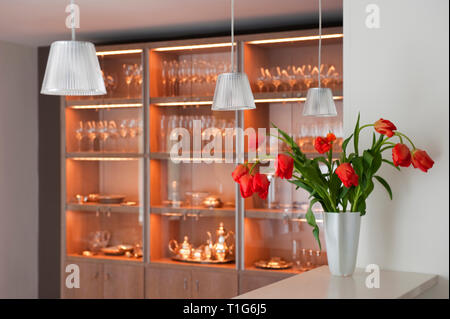 Vase of red flowers on counter by shelves of glassware Stock Photo