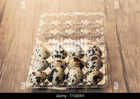 Quail eggs in plastic container on brown wooden background. Stock Photo