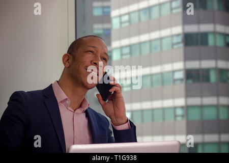 Happy office worker making a phone call at his computer Stock Photo
