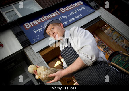 Champion haggis maker John Potter, who relocated from his native Scotland to Merseyside, with freshly-made haggis outside Braveheart Butchers which he owns in Wallasey, Wirral. Haggis is a dish containing sheep's 'pluck' (heart, liver and lungs), minced with onion, oatmeal, suet, spices, and salt, mixed with stock, and traditionally boiled in the animal's stomach for approximately three hours. It is a traditional Scottish dish usually served with 'neeps and tatties' (swede, yellow turnip and potatoes, boiled and mashed separately) and a 'dram' of Scotch whisky), especially as the main course o Stock Photo