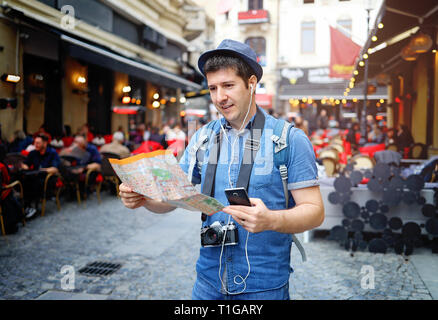 Backpacker Traveler Man traveling alone on crowded streets in old town. Neck camera and holding city map in hand. Travel Europe Stock Photo