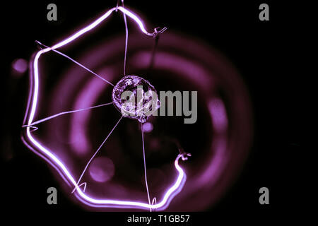 A  macro photography of an old fashion glass light bulb in purple hue in black background Stock Photo